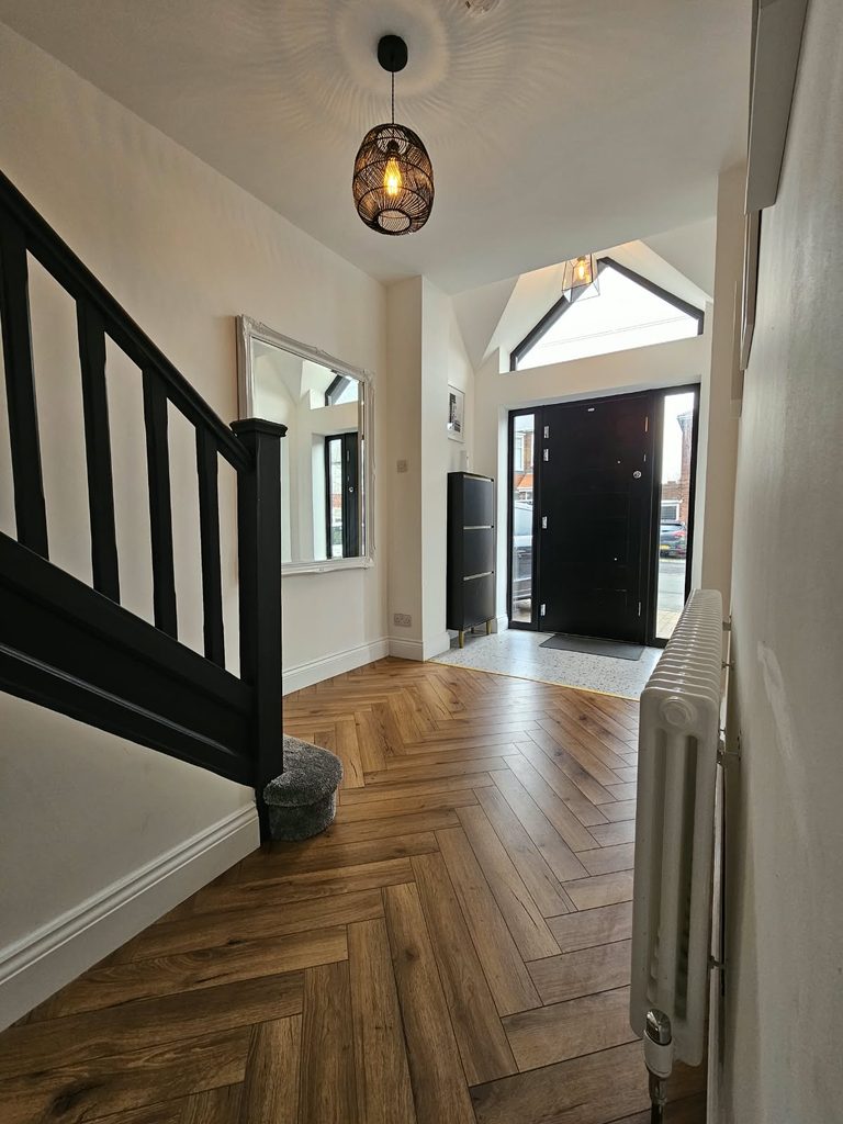 Hallway with herringbone flooring, terrazzo-effect entrance tiles and a black-painted staircase beneath the glazed gable