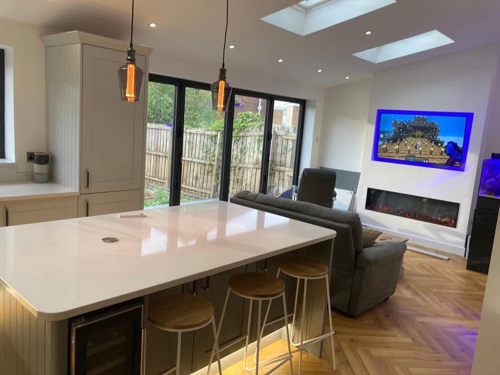 Inside the kitchen extension in Monkseaton: a white-topped island, bi-fold doors to the garden, roof lights and a media wall