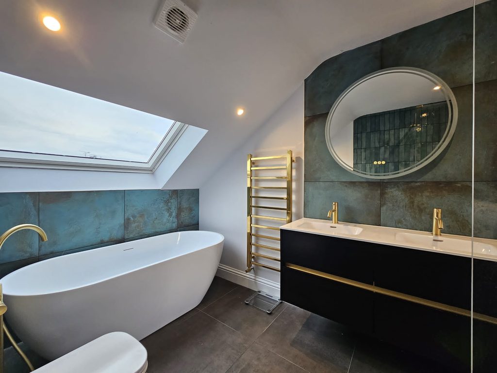 Loft en-suite looking towards a freestanding bath under a rooflight, with brushed brass taps and a double vanity
