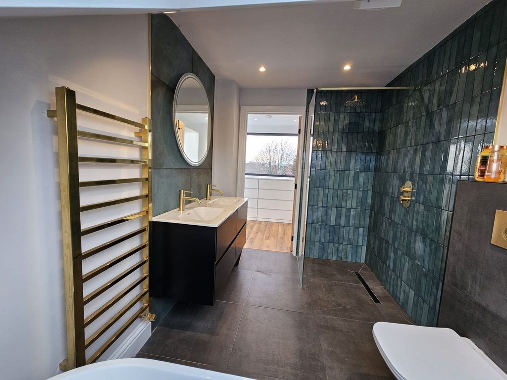 Loft en-suite with a brass towel rail, double vanity and walk-in shower lined in teal tiles