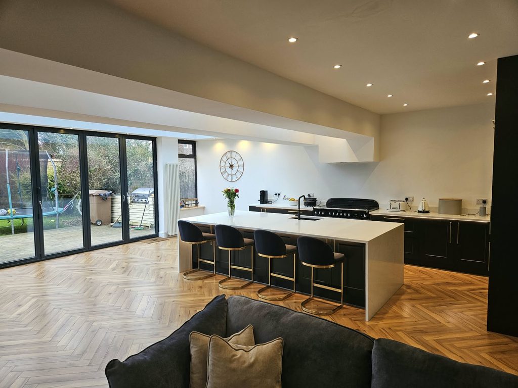 Open-plan kitchen with dark shaker units, a white waterfall island seating four and herringbone flooring