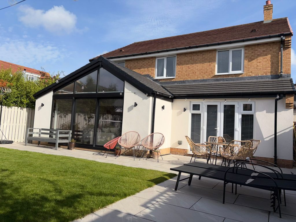 Rear of the house after the work, with the gable-ended kitchen extension, white render and a porcelain patio