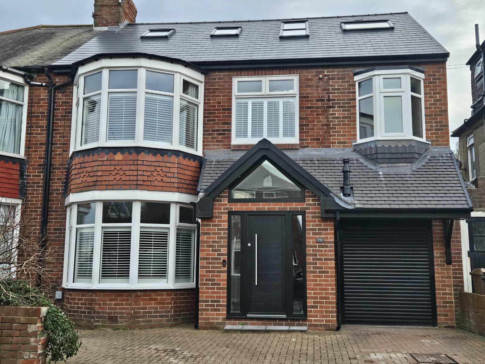 Front of the house after the two-storey side extension, with a gabled glazed porch, roller garage door and four rooflights
